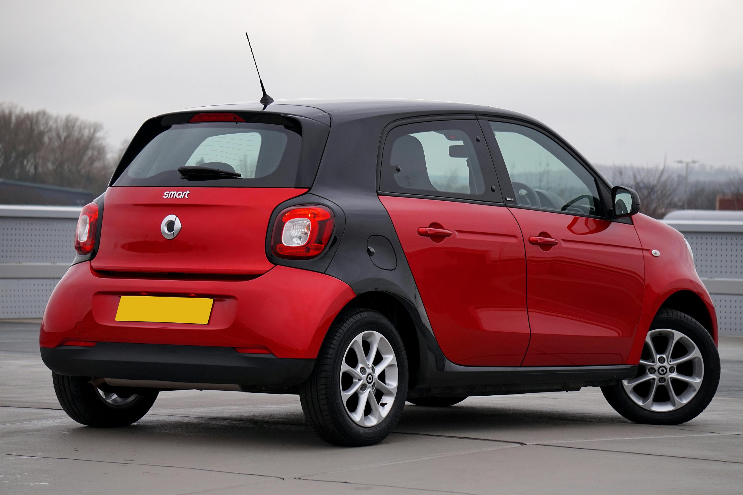 Rear view of a red Smart Forfour parked outdoors on a cloudy day, showcasing sleek design.