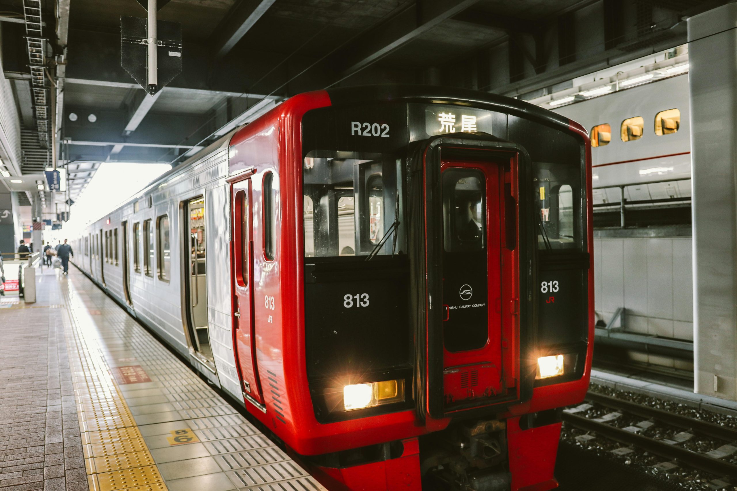 A sleek red train at an urban railway station platform during the day, ready for departure.